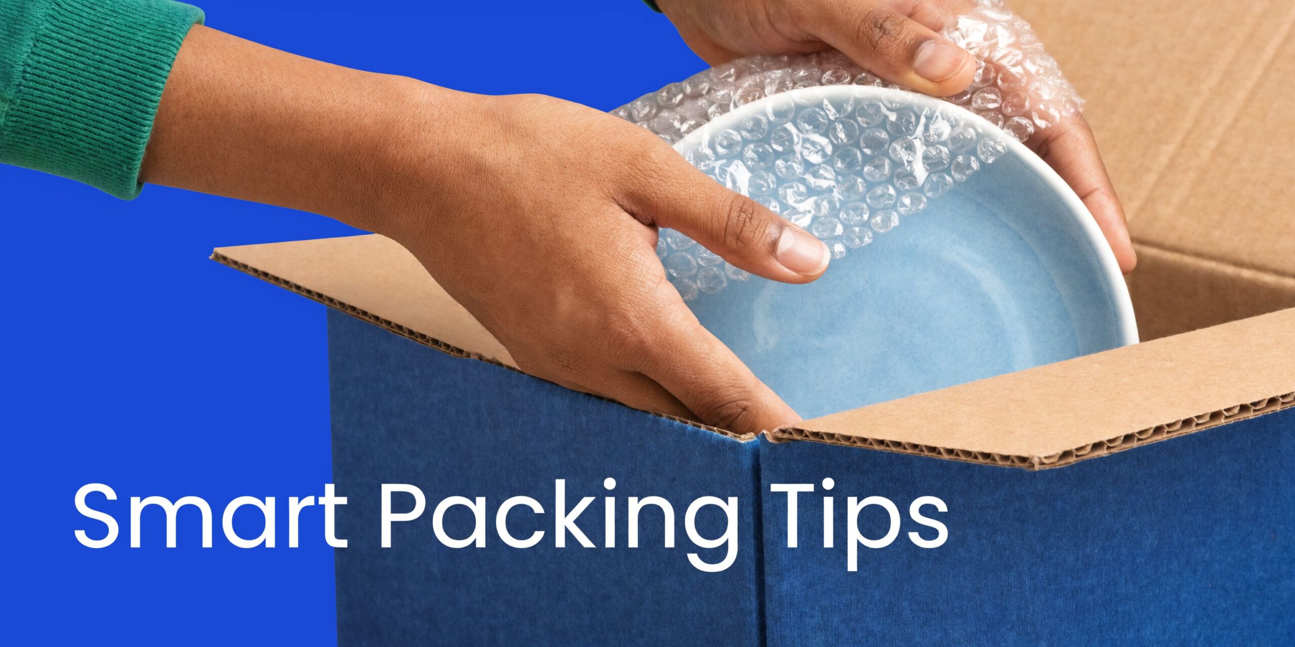 A pair of hands carefully packing a blue ceramic bowl with bubble wrap into a cardboard box.