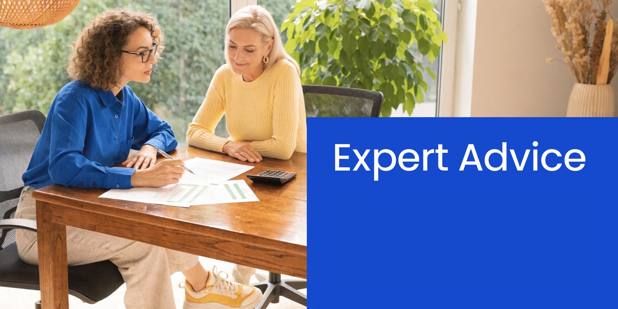 A professional financial advisor reviews documents with a client at a wooden table in a home office.