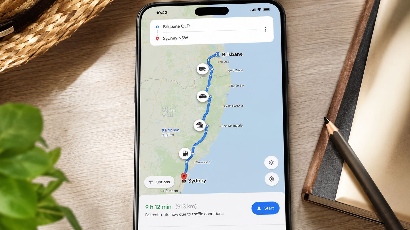 A smartphone screen displaying a Google Maps route from Brisbane to Sydney on a wooden desk.