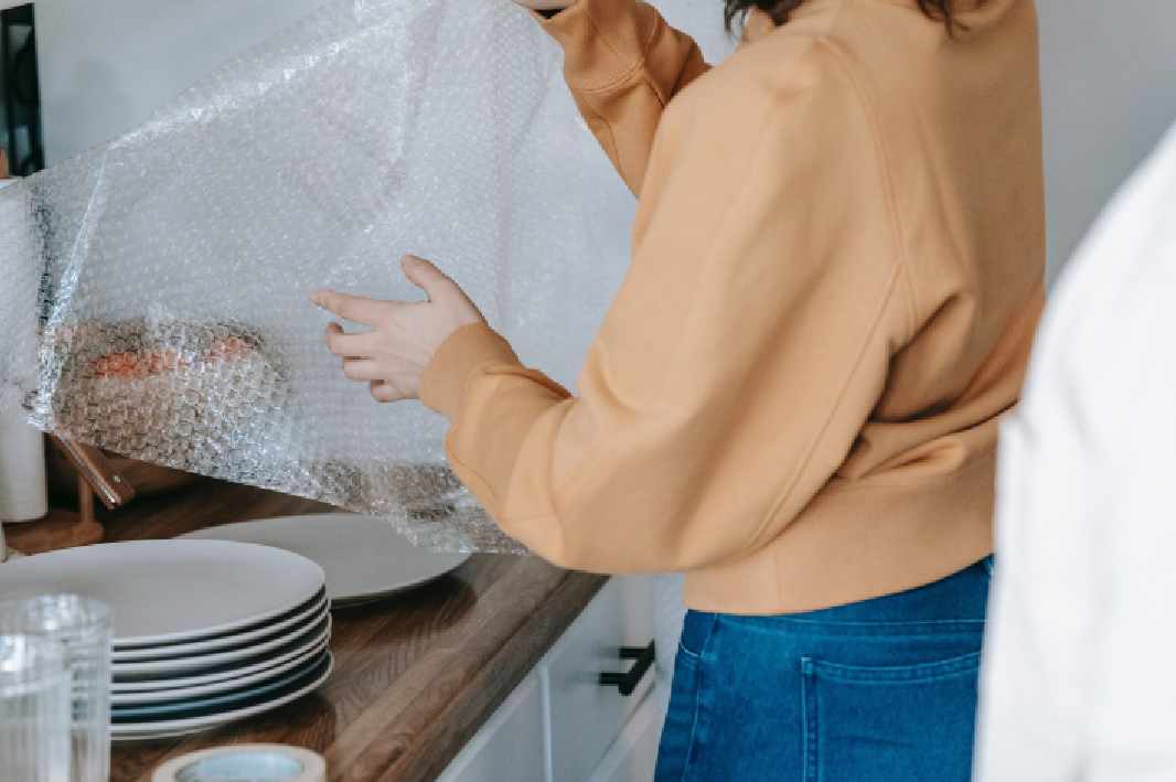 women packing plates in kitchen using bubble wrap